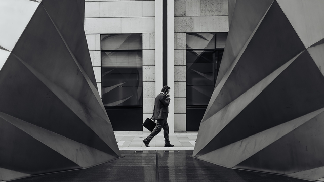 A black and white image of a business man on a phone by a scuplture